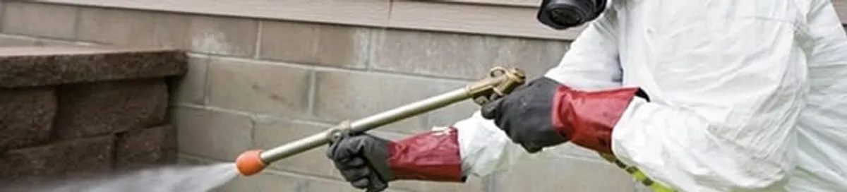 Pest control technician applying exterior insect treatment along a home foundation in New Orleans, LA