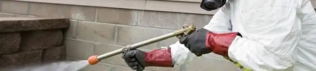 Pest control technician applying exterior insect treatment along a home foundation in New Orleans, LA