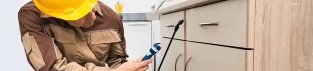 Roach exterminator applying treatment under kitchen cabinets in New Orleans, LA