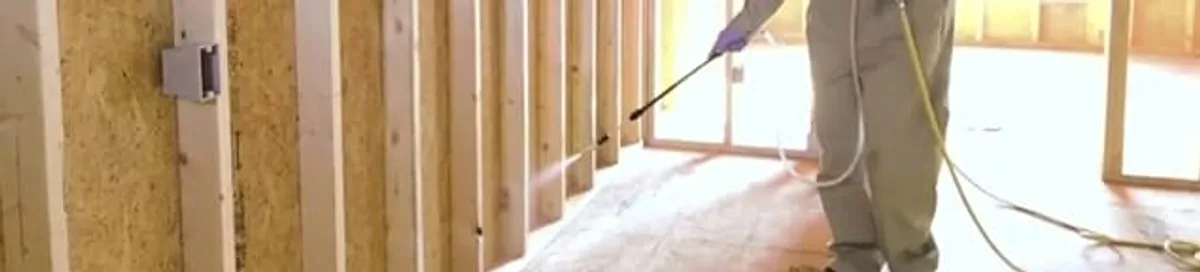 Termite treatment technician applying spray along framing and unfinished walls in New Orleans, LA